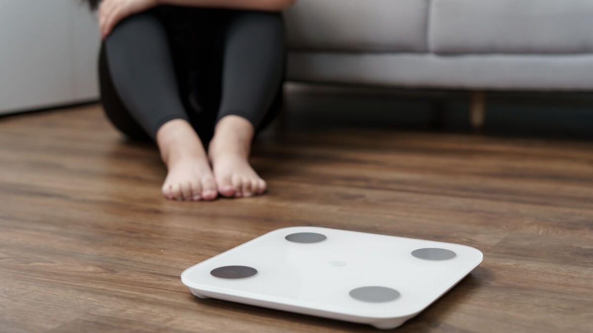 Bathroom scale on the floor with a person resting nearby, symbolizing assessing fitness progress with awareness.