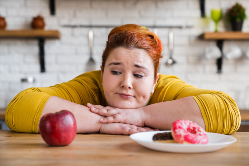 why most diets fail woman looking at a donut and an apple