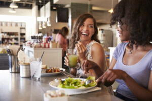 Two women enjoying a healthy dinner with salads, representing sustainable eating habits instead of dieting.