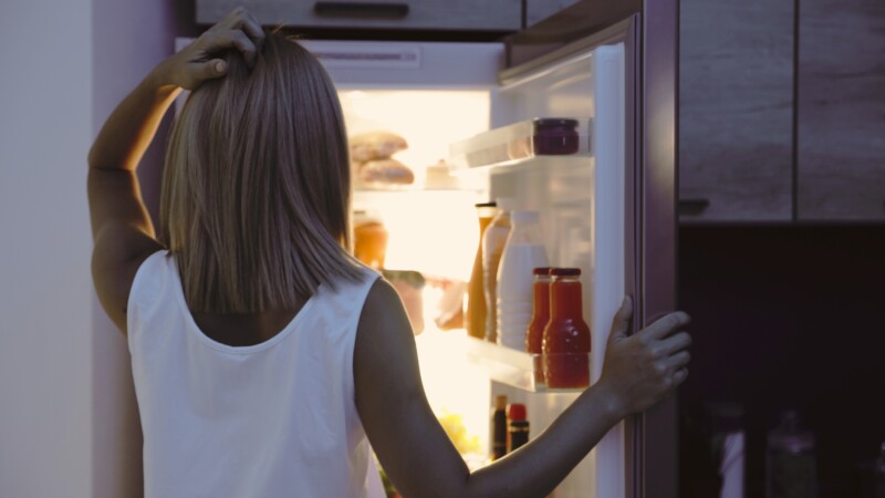 Woman standing at an open refrigerator at night, deciding what to eat after a long day. healthy choices at night