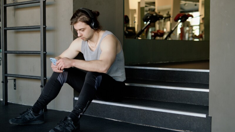 Man in a gym looking at his phone, representing lack of structure in a workout routine.